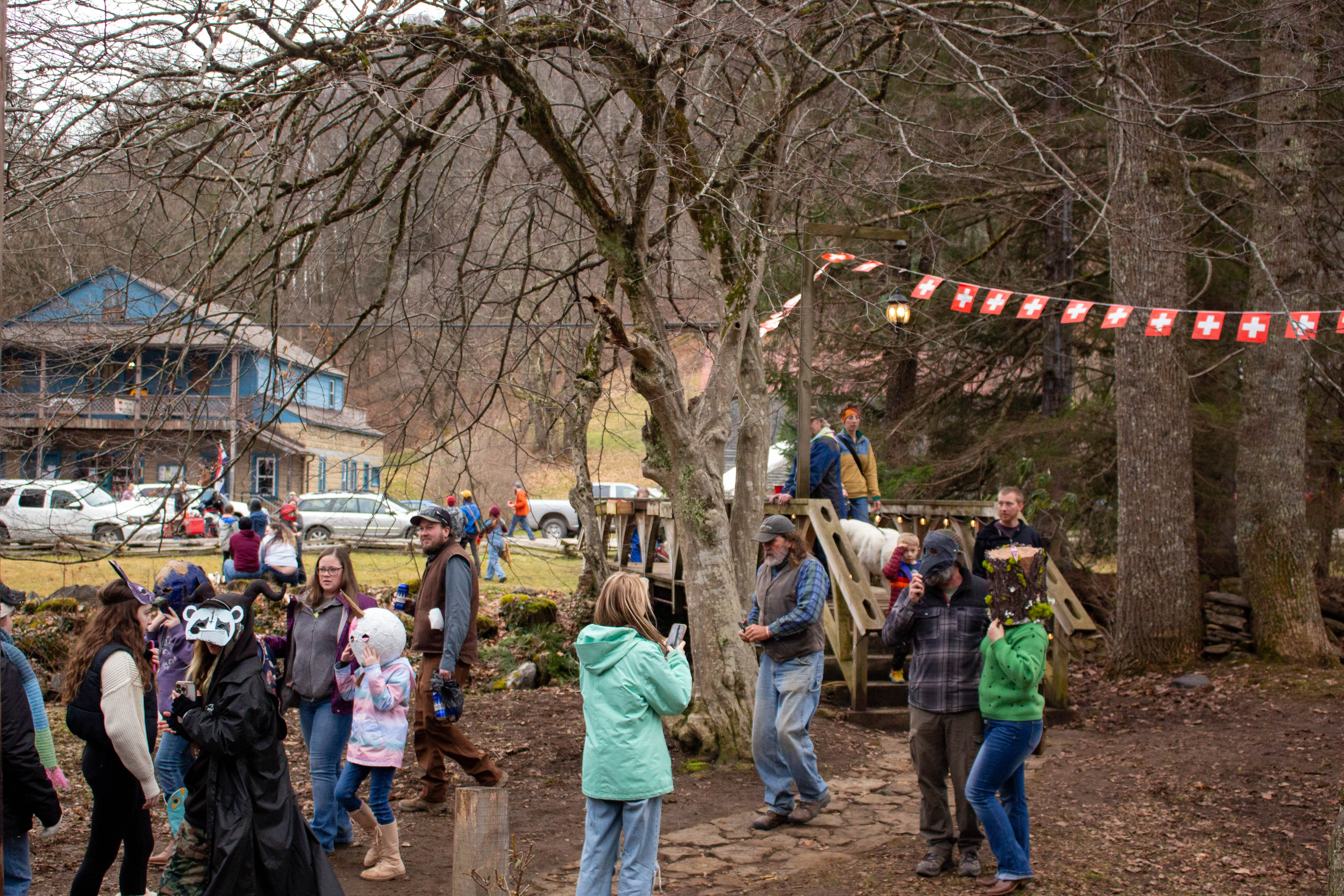 People walk outside, some wearing masks. A walking bridge with lights and a line of Swiss flags over head is visible. The road with cars and a blue building in the background.
