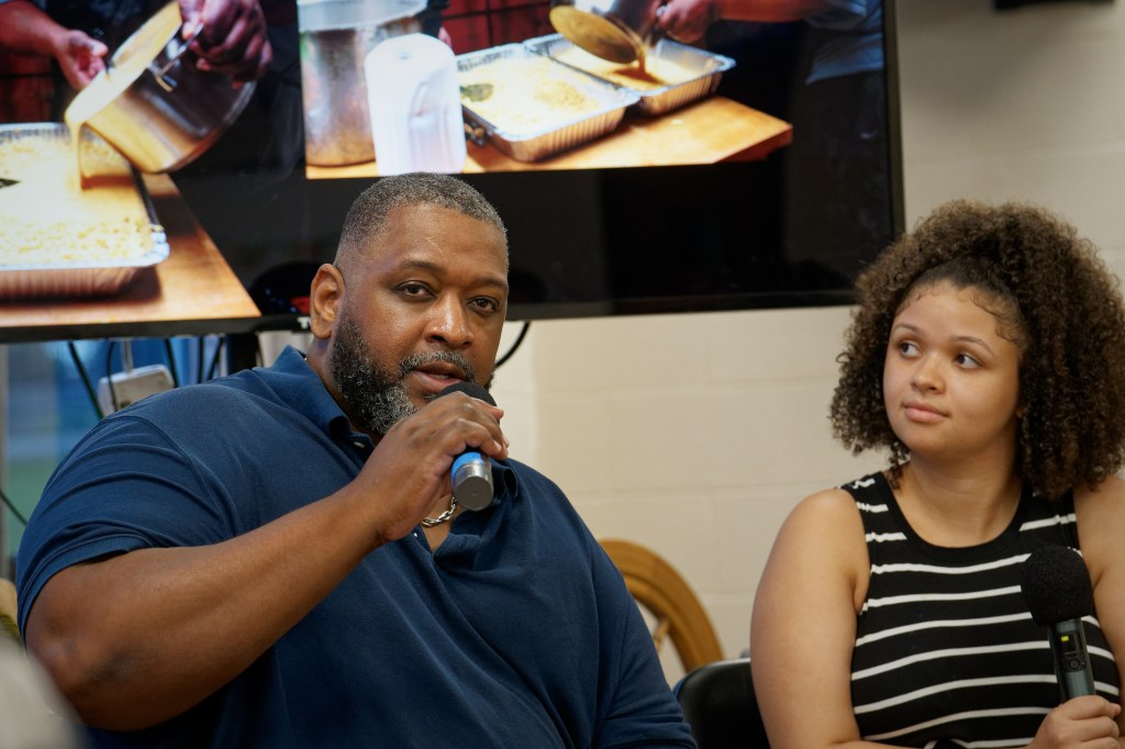 A Black man and a younger woman sit together, both holding microphones.