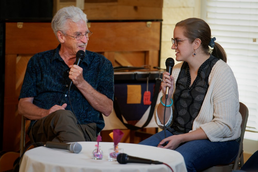 An older man and younger woman sit together speaking into microphones.