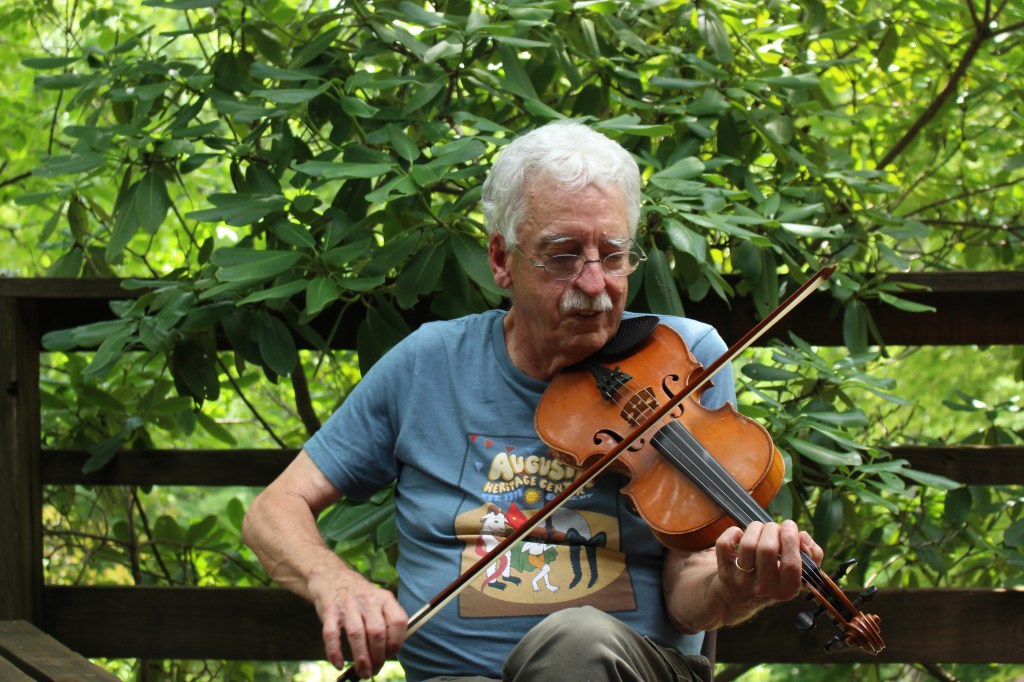 An older man plays fiddle outside.