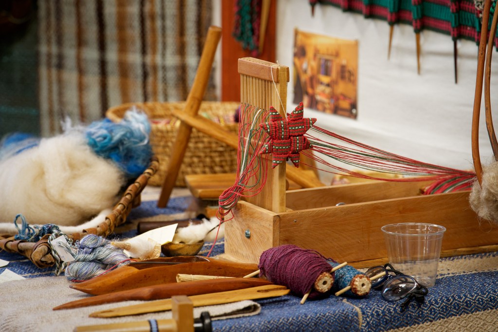 A display of weaving tools including a table loom and various shuttles and spools made from corn cobs.