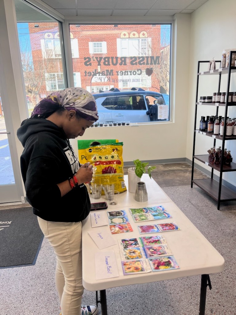 A woman stands beside a table, and bags of seeds and soil are on the table.