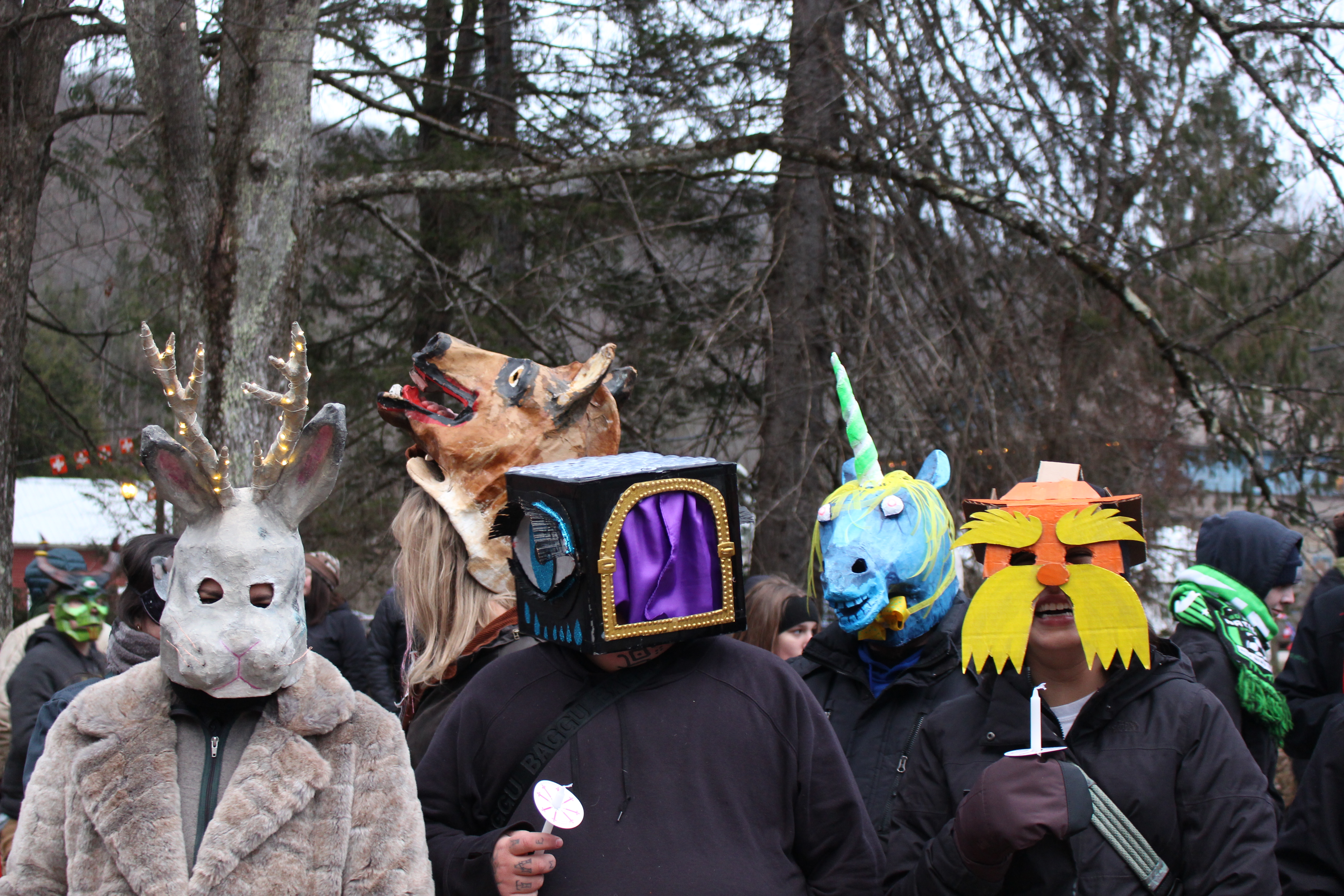 A group of people wearing costumes stand outside together. Costumes include a jackalope, a horse, a unicorn, a box with a curtain, and the Dr. Seuss character The Lorax.